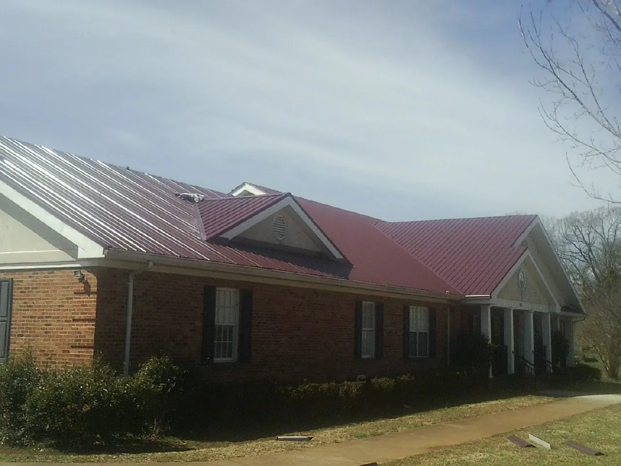 Red metal roof with gabled entries on a long brick building, from a Hail Damage Roof Repair job in Sumava Resorts