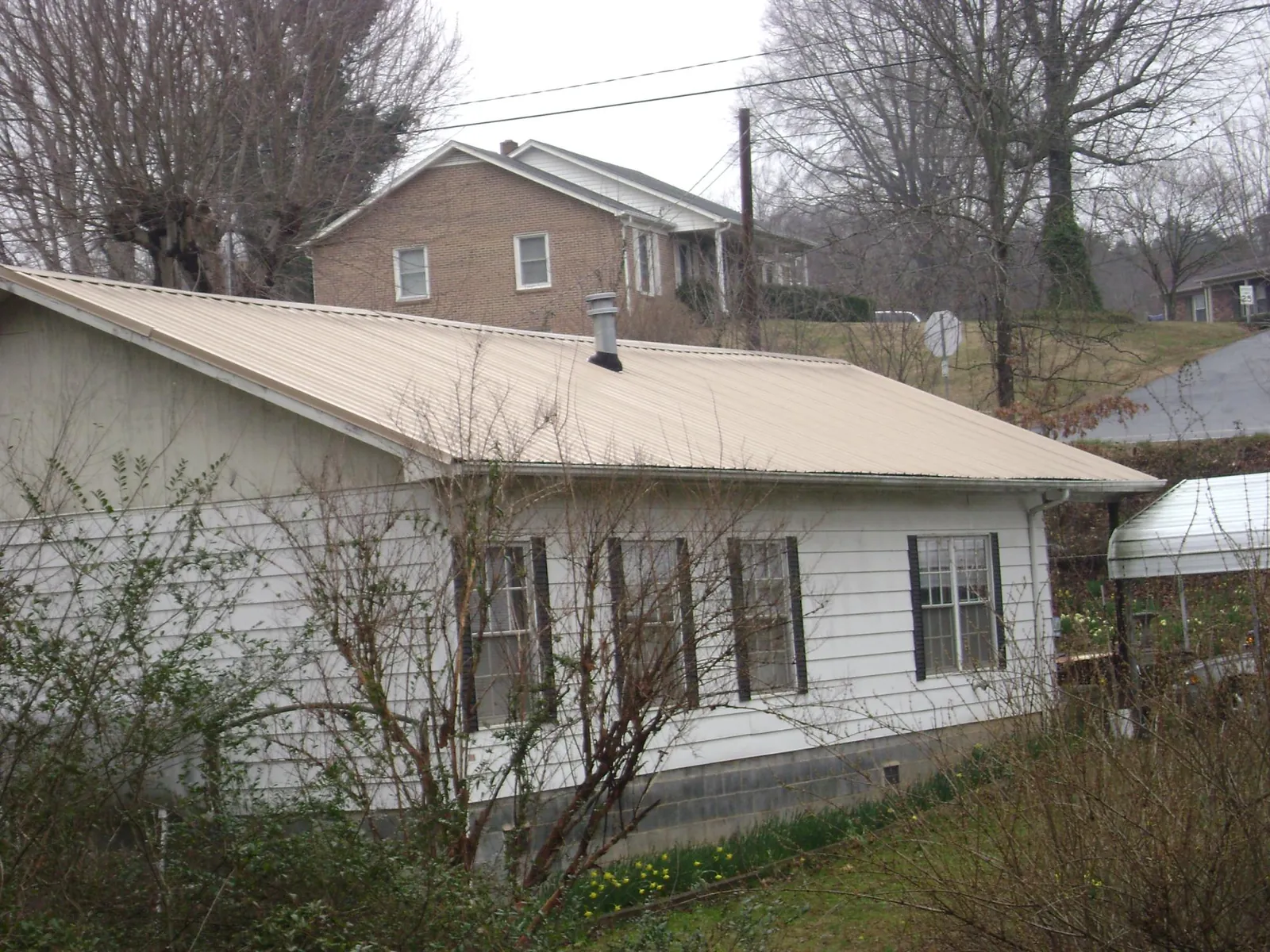 Tan metal roof on a white sided house set into a hillside — Commercial Roofing by Roofing Brothers in Sumava Resorts